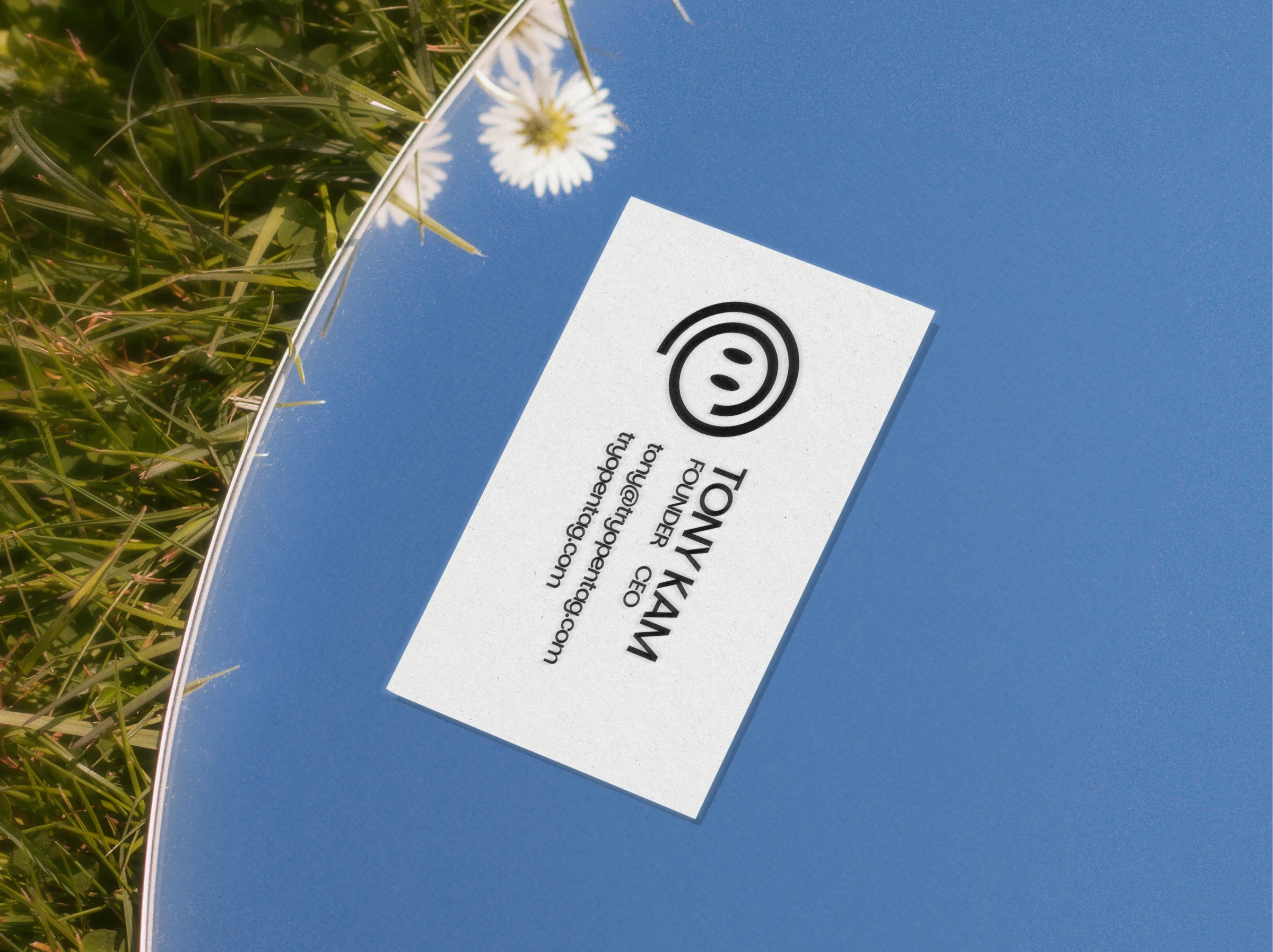 Opentag business card for Tony Kam, founder, lying on a mirror in the grass