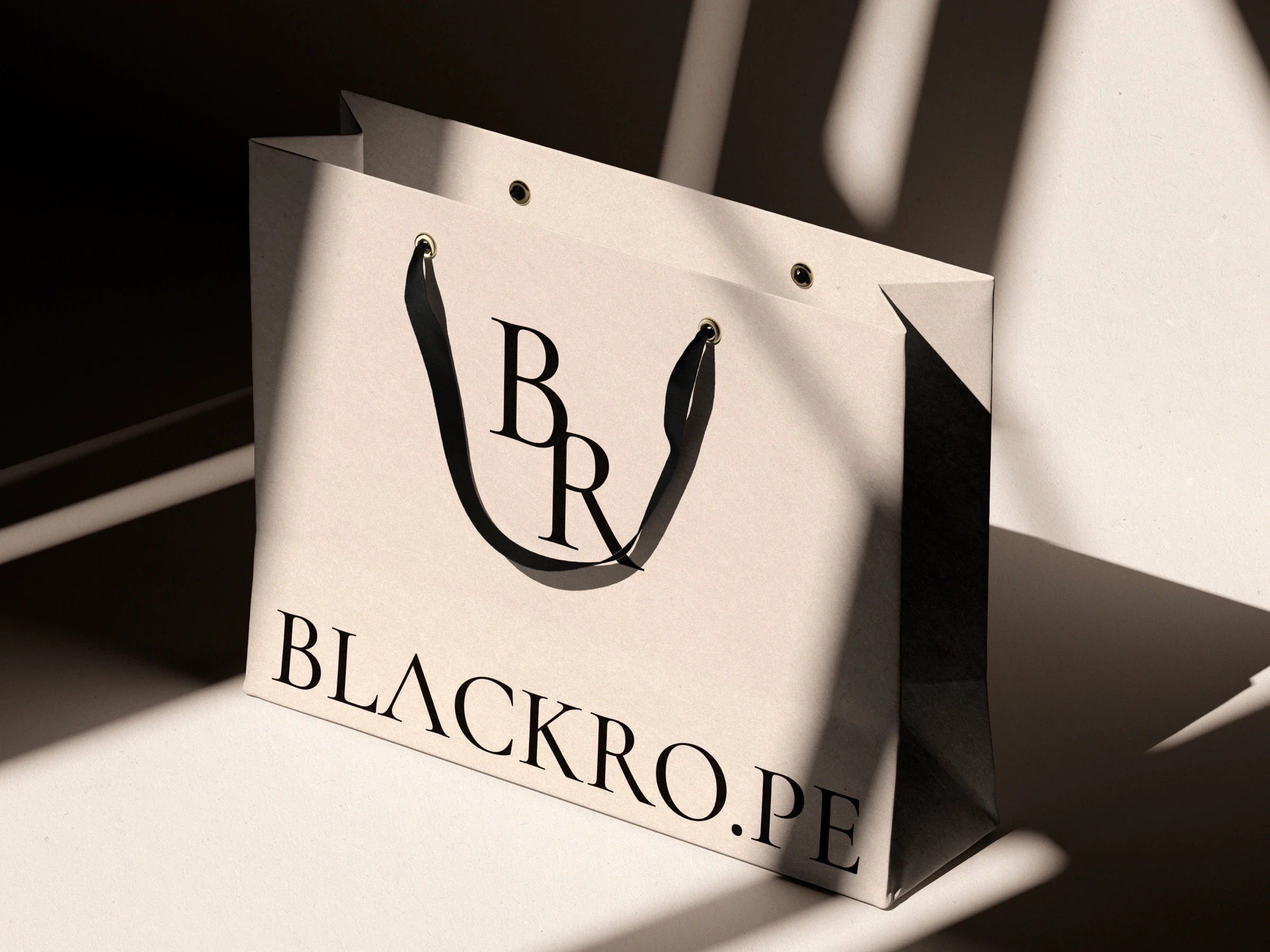 A white paper bag with the serif monogram and wordmark in raking sunlight